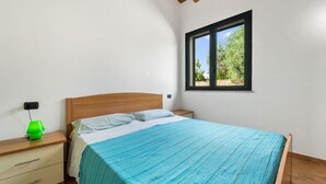 Una camera da letto con un letto, un comodino, una lampada e una finestra vista alberi.
