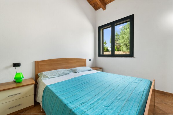 A bedroom with a bed, a nightstand, a lamp, and a window with a view of trees.