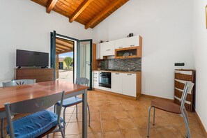 A compact kitchen with white cabinets, a stone backsplash, and a dining area with a wooden table and chairs.