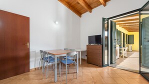Una stanza con soffitto in legno, un tavolo da pranzo con sedie, una TV e una porta scorrevole in vetro che dà su uno spazio all'aperto.