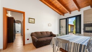 A dining area with a table and chairs, a sofa, a wooden ceiling, and a view through a glass door. - Holiday Home Residence Sulcis 7 with Shared Terrace & A/C (Masainas)