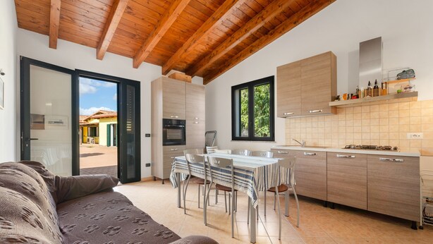 A modern kitchen with a dining area, wooden ceiling beams, and a view through the door. - Holiday Home Residence Sulcis 7 with Shared Terrace & A/C (Masainas)