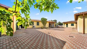 A courtyard with a tiled floor, a cactus, and yellow buildings with green shutters. - Holiday Home Residence Sulcis 7 with Shared Terrace & A/C (Masainas)