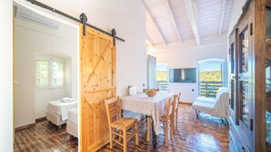 A room with a wooden floor, a dining table with chairs, a bed, and a sliding barn door. - Villa Adamantia Paxos with Pool, Terrace & Wi-Fi (Paxos)