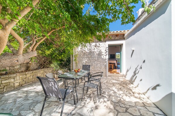 An outdoor patio with stone flooring, a table with chairs, and a tree providing shade.