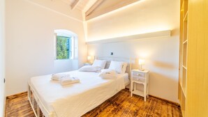 A bedroom with a bed, bedside tables, a window, and a wooden floor. - Villa Adamantia Paxos with Pool, Terrace & Wi-Fi (Paxos)