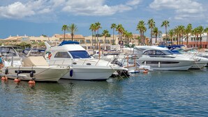 Un puerto deportivo con varias embarcaciones amarradas, palmeras al fondo y edificios con letreros.
