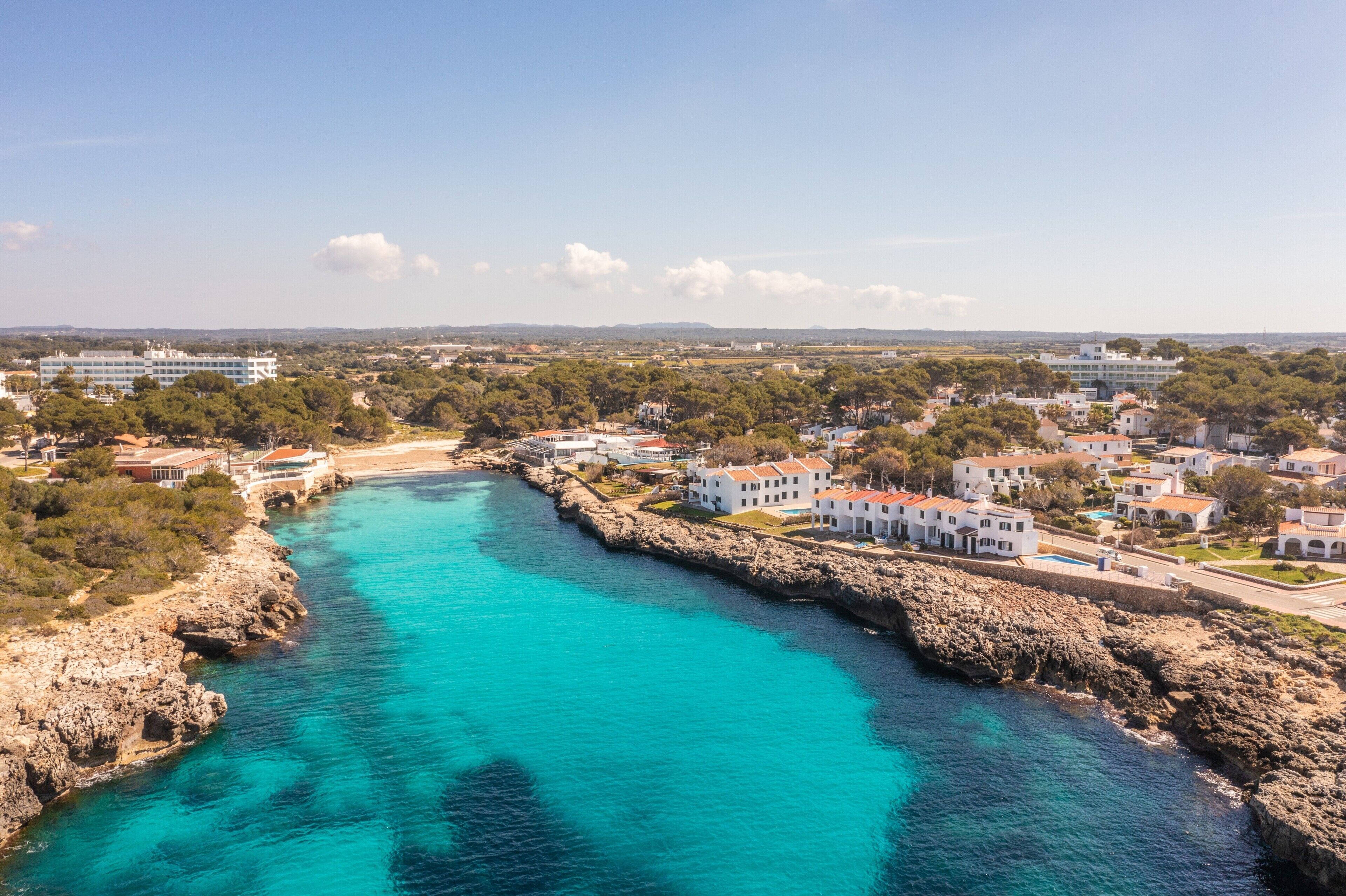 A coastal town with a turquoise bay, white buildings, and rocky cliffs.