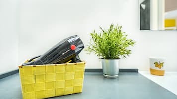 En gul fletkurv med en sort genstand på en grå bordplade, en potteplante og en hvid kop med et gult mønster.