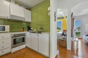 Une cuisine avec des armoires blanches, un four encastré, un four à micro-ondes, un évier et un plan de travail recouvert de carreaux verts.