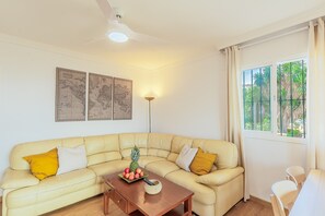 Un salon avec un canapé beige, une table basse en bois, un globe terrestre et une fenêtre donnant sur un paysage verdoyant.
