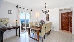 Comedor con mesa, sillas, candelabro, vista a través de un ventanal y puerta de madera.