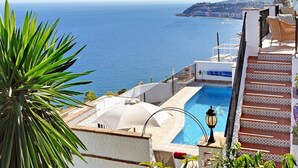Una piscina con vista al mar, una escalera con baldosas estampadas y un farol.