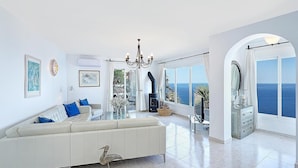 Un salón amplio con un sofá grande, una chimenea y vistas al mar.
