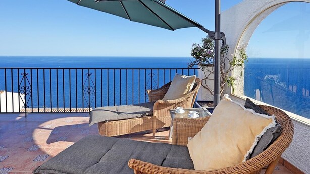 Un balcón con sillas de mimbre, una mesa con tazas y vista al mar.