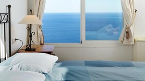 Un dormitorio con cama, mesita de noche, lámpara y vista al océano.