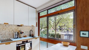 A modern kitchen with a large window, a white countertop, and a wooden table. - UK.LO.DCR - Spacious 1 bedroom apartment in Kennington (London)