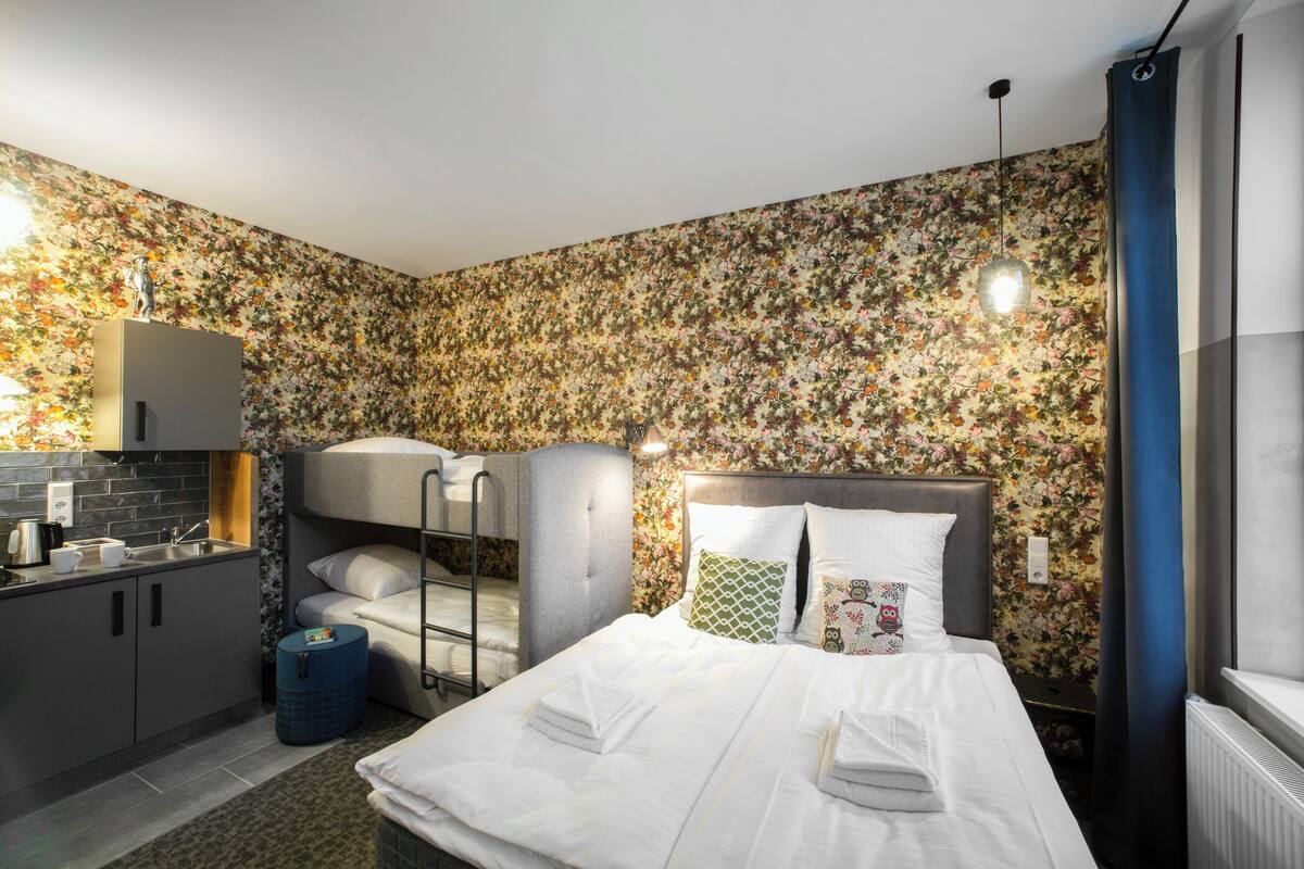 Habitación de hotel compacta con literas, un pequeño rincón americano y una cama con toallas ordenadas.