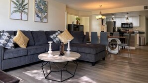 A modern living room with a sectional sofa, a round coffee table, and a dining area with a kitchen in the background. - Grand Luxury 3BR Condo near Disney Universal #12 (Kissimmee)