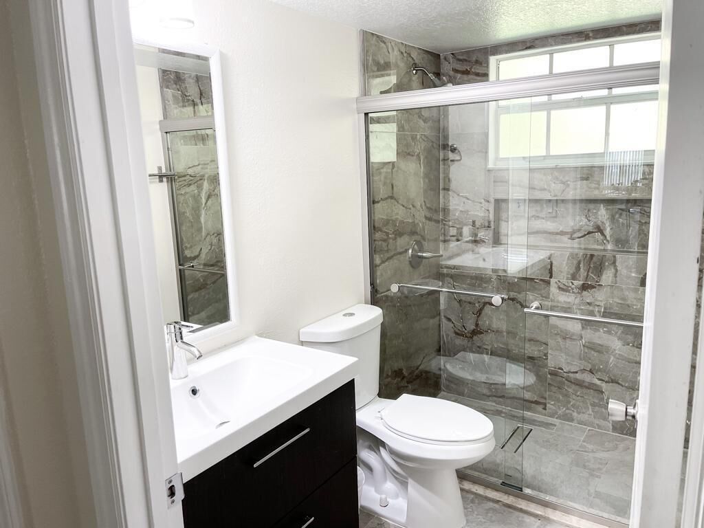 A bathroom with a glass-enclosed shower, a white sink, and a toilet.