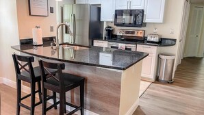 A modern kitchen with a large island, white cabinets, stainless steel appliances, and a hanging pendant light. - Grand Luxury 3BR Condo near Disney Universal #12 (Kissimmee)
