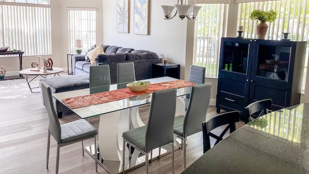 A modern living room with a glass dining table, grey sofas, and a dark blue cabinet. - Grand Luxury 3BR Condo near Disney Universal #12 (Kissimmee)