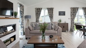A living room with a sofa, a coffee table, a TV, and a fireplace. - Hazel Lodge, 27 Roadford Lake Lodges (Lifton)