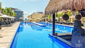 Un área de piscina con sillones de descanso, sombrillas y una estructura de techo de paja.