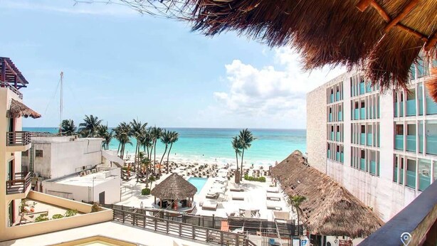 Un resort con zona de piscina, vista a la playa y construcciones de techo de paja.
