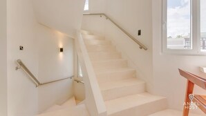 Un escalier avec des marches blanches et des rampes en métal, menant à un palier doté d’une fenêtre.