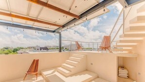 Une vaste terrasse sur le toit, dotée d’un escalier moderne, d’un fauteuil de relaxation en bois et offrant une vue dégagée sur le panorama urbain.