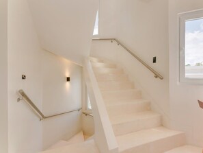 A staircase with white steps and metal handrails, leading to a landing with a window.