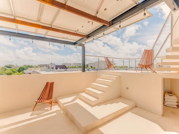 Een ruim terras op het dak met een moderne trap, een houten lounge stoel en een helder uitzicht op de stadshemel.