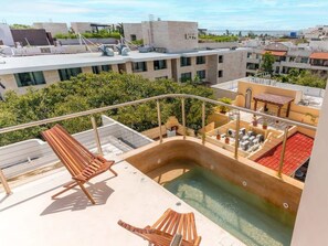 A rooftop pool area with two wooden loungers, a small table, and a hot tub. - 5th Ave Rooftop Pool with Ocean Views and BBQ (Playa del Carmen)