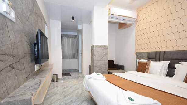 A modern hotel room with a large bed, marble flooring, a TV mounted on the wall, and a unique hexagonal wall pattern. - Hotel A1 Vastrapur (Ahmedabad)
