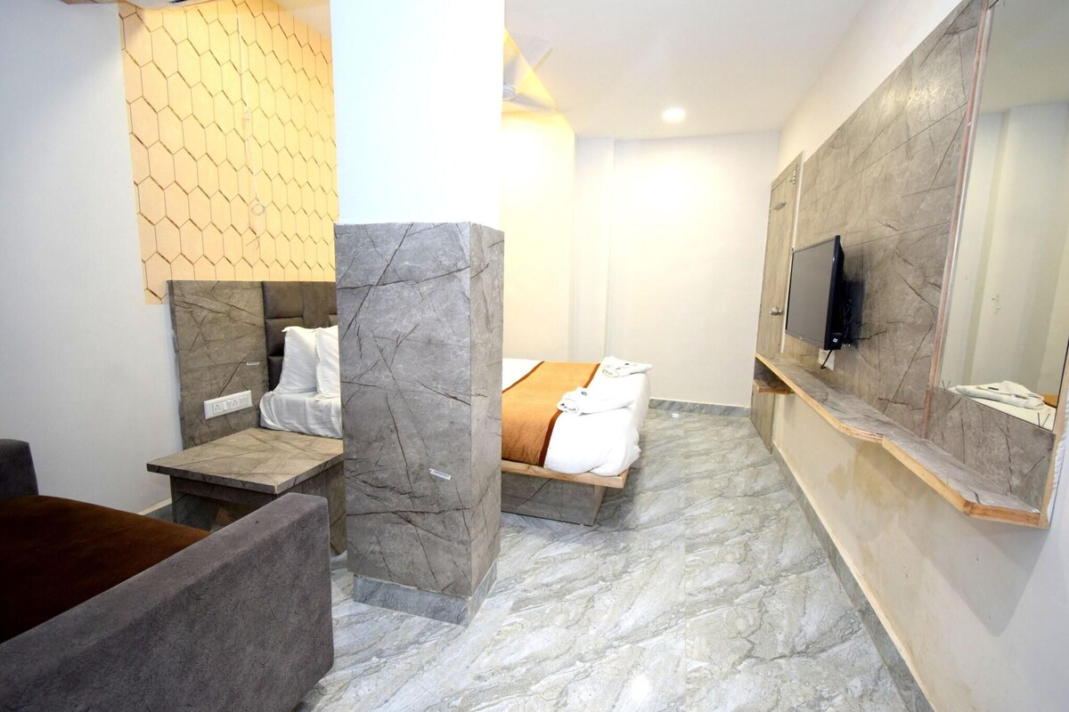 A modern bathroom with a marble floor, a bed with white linens, a wooden bench, and a mounted TV.
