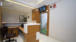 A reception desk with a wooden finish, a black office chair, and a flat-screen TV mounted on the wall. - Hotel A1 Vastrapur (Ahmedabad)