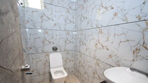 A bathroom with a toilet, a sink, and marble walls. - Hotel A1 Vastrapur (Ahmedabad)