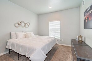 A bedroom with a bed, a window with blinds, a wall-mounted artwork, and a small table with a lantern.