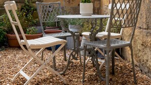 Eine Terrasse mit rundem Tisch und vier Stühlen, umgeben von Kübelpflanzen und einer Steinmauer.