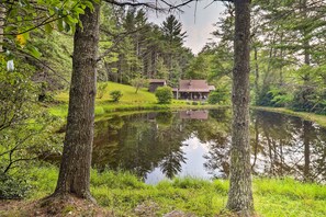 A cabin with a pond in front, surrounded by trees and greenery. - Rustic Cabin w/ Patio & Pond on Blue Ridge Parkway (Ennice)