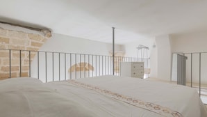Ein Schlafzimmer mit einem großen Bett, einer Steinwand, einem Metallgeländer und einem Fenster.