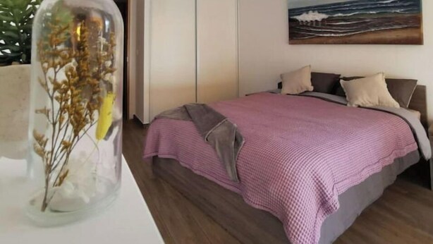 Et soveværelse med seng, et billede, en garderobe og en dekorativ glasflaske.
