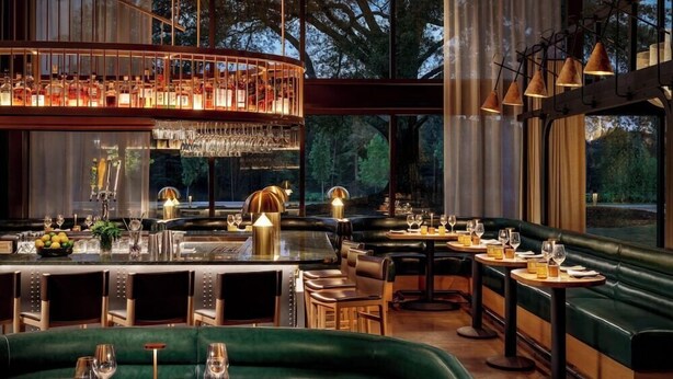 A restaurant with a bar area, green seating, and large windows. - Hotel Hartness (Greenville)