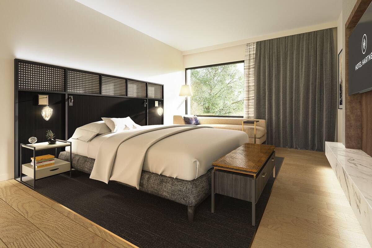 Ein modernes Hotelzimmer mit einem großen Bett, Nachttischen, einem Schreibtisch und Blick ins Freie.