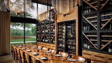 A restaurant with a long wooden table set for dining, wine racks, and hanging lights.