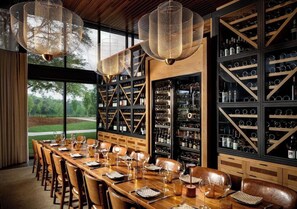 A restaurant with a long wooden table set for dining, wine racks, and hanging lights. - Hotel Hartness (Greenville)