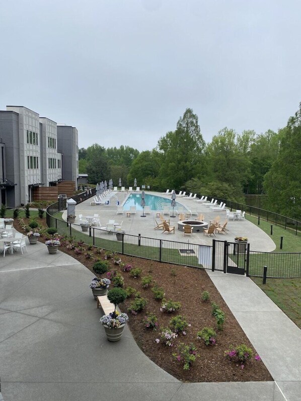 A pool area with lounge chairs and umbrellas, surrounded by a fence and potted plants. - Hotel Hartness (Greenville)
