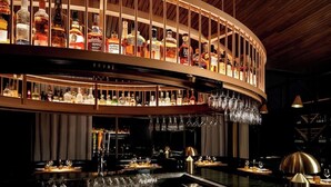 A bar with multiple shelves of liquor bottles and hanging glasses. - Hotel Hartness (Greenville)