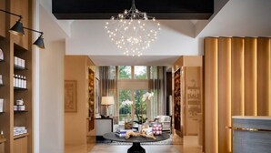 A modern interior with a central chandelier, wooden shelving, a round table with decorative items, and a view through a window. - Hotel Hartness (Greenville)
